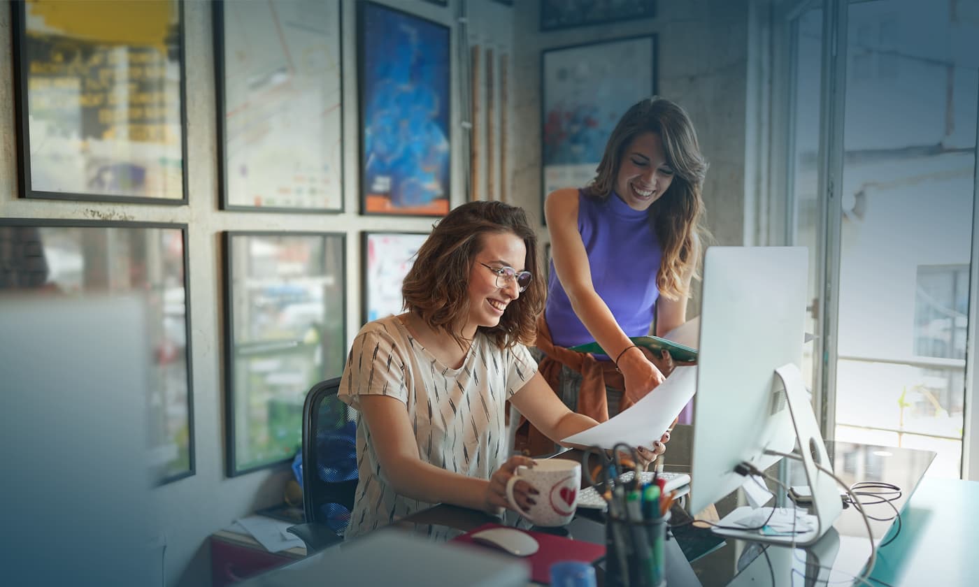 woman smiling with the other woman while looking at a paper