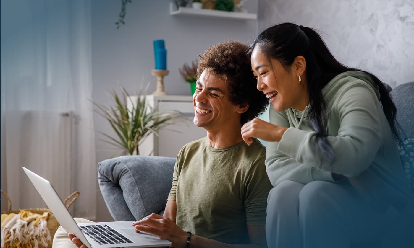 two people laughing while looking at laptop