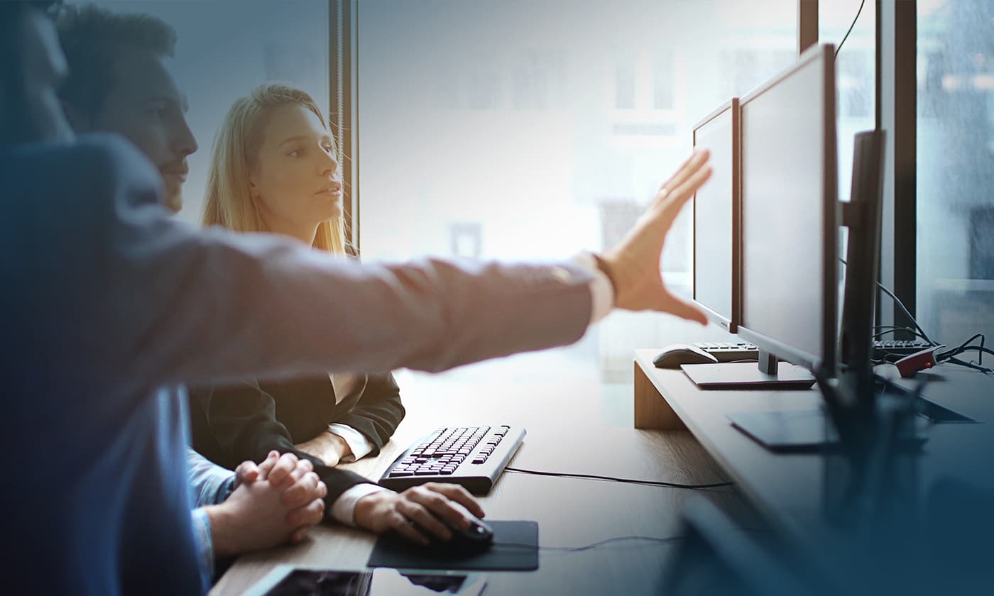 coworkers looking at computer monitors as one explains something to the others