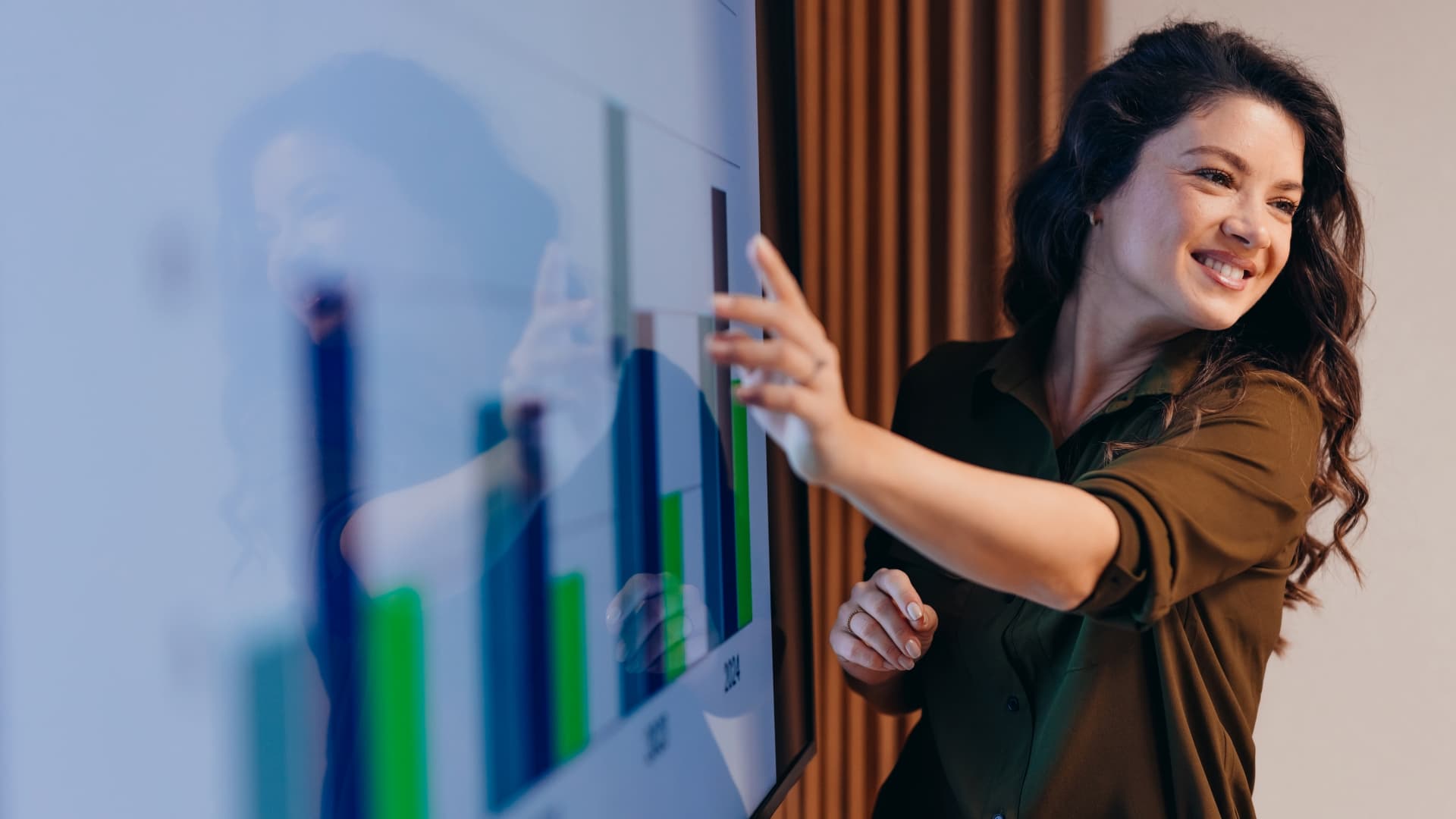 Woman smiling and pointing at a large screen displaying bar charts during a presentation